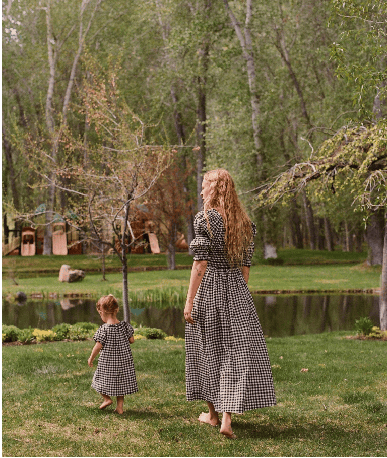 Woman and child in matching dresses standing in a park by a pond.